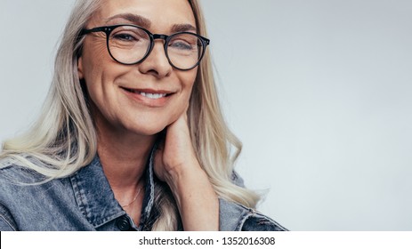 Relaxed senior caucasian female with eyeglasses looking at camera and smiling. Positive senior woman against grey background. - Powered by Shutterstock