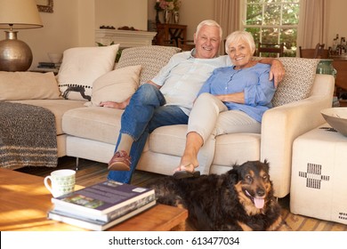 Relaxed Senior Couple Sitting Together On Their Vintage Looking Living Room Couch With The Family Dog At Their Feet