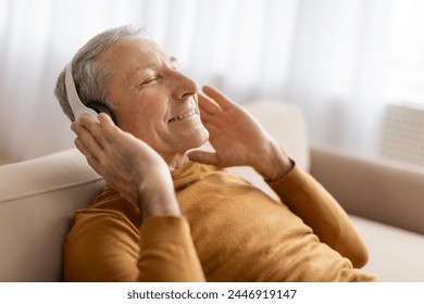 A relaxed senior man unwinding on a couch with a closed eyes, using wireless headphones, listening to music - Powered by Shutterstock