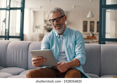 Relaxed senior man using digital tablet and smiling while sitting on the sofa at home - Powered by Shutterstock