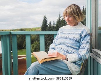 Relaxed senior woman is reading a book at a house balcony - Powered by Shutterstock