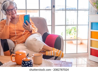 Relaxed senior woman sitting at home on armchair using smartphone, listening to music - Powered by Shutterstock