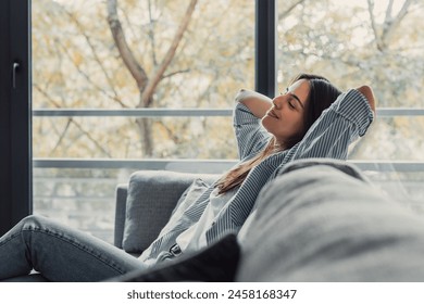 Relaxed serene pretty young woman feel fatigue lounge on comfortable sofa hands behind head rest at home, happy calm lady dream enjoy wellbeing breathing fresh air in cozy home modern living room - Powered by Shutterstock