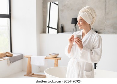 Relaxed serene young woman girl in bath spa towel and bathrobe drinking water hot beverage after shower bath at home. Stress relief concept. Beauty treatment