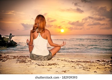 A relaxed sexy young brunette woman sitting on a deserted tropical beach at sunset 