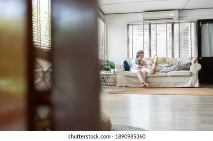 Relaxed smiling Asian Senior Couple sitting on sofa at home together. Romantic Chinese Grandfather and Grandmother reading a book on comfortable couch, Lover concept