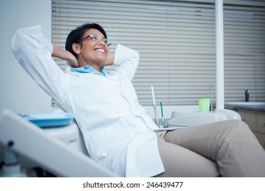 Relaxed smiling female dentist sitting on chair with hands behind head