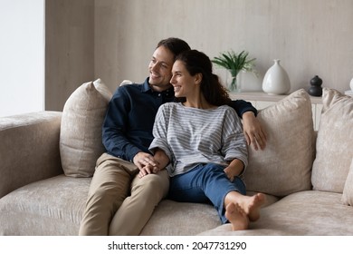 Relaxed Smiling Millennial Generation Hispanic Latin Family Couple Looking In Distance, Daydreaming Enjoying Stress Free Leisure Time Together At Own Home, Meditating Sitting On Comfortable Sofa.