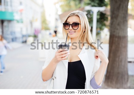 Relaxed stylish businesswoman drinking coffee outside on urban background