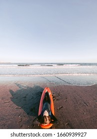 Relaxed Surfer In Wetsuit Sitting On The Surfboard On The Beach. View From Above. Image Made On Mobile Phone