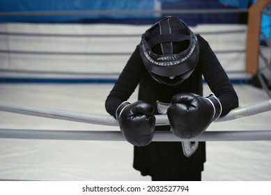 Relaxed Tired Exhausted Female Boxer Lying On The Ropes Of Ring. Woman In Hijab Rest After Hard Training.