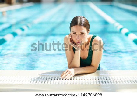 Relaxed wet woman in swimwear leaning over edge of swimming-pool at spa resort