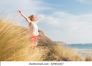 Relaxed woman, arms rised, enjoying sun, freedom and life an a beautiful beach. Young lady feeling free, relaxed and happy. Concept of vacations, freedom, happiness, enjoyment and well being.