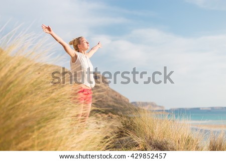 Relaxed woman, arms rised, enjoying sun, freedom and life an a beautiful beach. Young lady feeling free, relaxed and happy. Concept of vacations, freedom, happiness, enjoyment and well being.