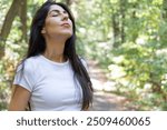 Relaxed woman breathing fresh air in a green summer forest and making breathing exercises 