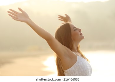 Relaxed woman breathing fresh air raising arms at sunrise with a warmth golden background - Powered by Shutterstock