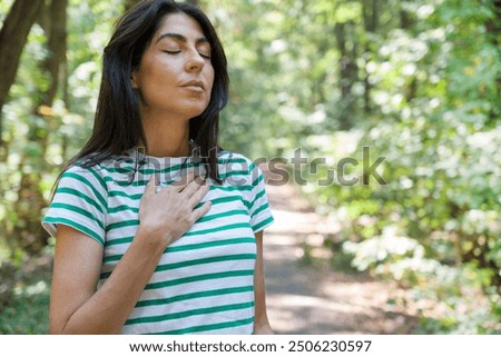 Relaxed woman breathing fresh air in a green summer forest and making breathing exercises 