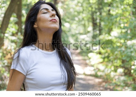 Relaxed woman breathing fresh air in a green summer forest and making breathing exercises 