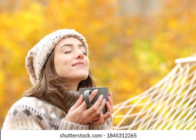 Relaxed woman breaths fresh air holding coffee cup for breakfast sitting on a rope hammock in autumn in a forest - Powered by Shutterstock