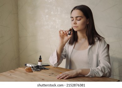 Relaxed Woman With Closed Eyes Smelling Aromatic Fragrance Of Natural Essential Oil From Glass Bottle While Enjoying Aromatherapy At Table At Home 