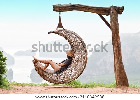Relaxed woman girl sit on the moon shape wooden swing with island and mountain lanscape view in Pang Nga, Samed Nangshe, Thailand
