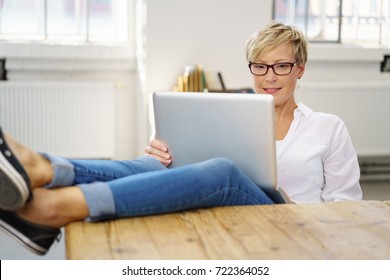 Relaxed woman with her feet on the table working on a laptop balanced on her knees with an absorbed expression