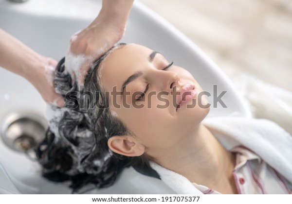 Relaxed. Woman looking relaxed while hair stylist\
washing her hair
