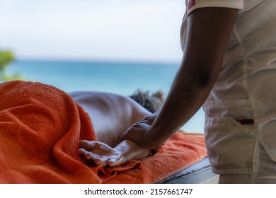 Relaxed Woman Lying Down Getting Massage Therapy In Caribbean Beach Spa With Copy Space