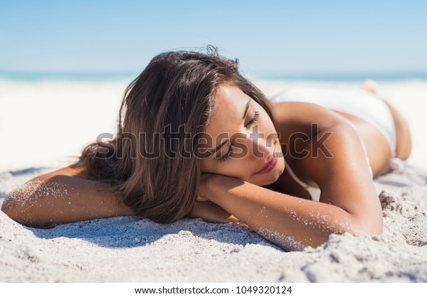 Relaxed woman lying down on sand during summer vacation.\
Beautiful girl lying down under the sun tanning in a tropical\
beach. Positive and serene young woman sunbathing at seaside with\
closed eyes. 