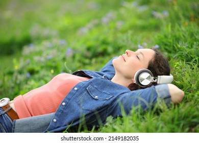 Relaxed woman lying on the grass listening to music with headphones in a park - Shutterstock ID 2149182035