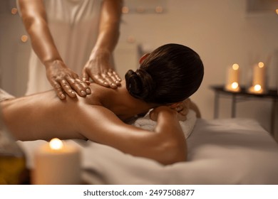 Relaxed woman lying on massage table while massage therapist massages her back, applying pressure to release tension in the woman muscles - Powered by Shutterstock