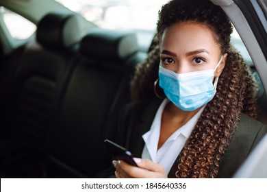 Relaxed Woman Passenger  In Protective Medical Mask In The Taxi Car On A Backseat With Phone. Work On The Way To The Office. Covid-2019.