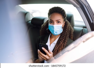 Relaxed Woman Passenger  In Protective Medical Mask In The Taxi Car On A Backseat With Phone. Work On The Way To The Office. Covid-2019.