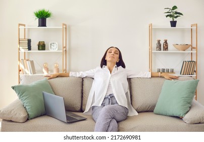 Relaxed woman resting on soft comfy couch at home, breathing deeply, enjoying peace, quiet and comfort. Happy lady sitting eyes closed on sofa in cosy light livingroom with stylish shelves in own flat