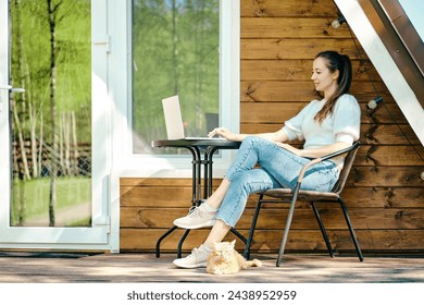 Relaxed woman sitting with laptop on terrace of log cabin in a sunny day - Powered by Shutterstock