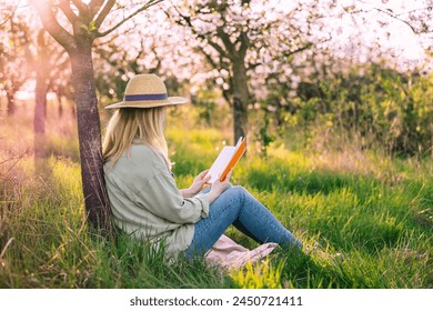 Relaxed woman sitting under blooming cherry tree and reading book to improve her mindfulness. Enjoying moments of solitude and relaxation in spring orchard - Powered by Shutterstock