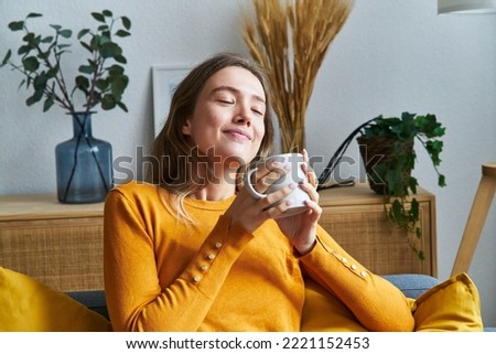 Relaxed woman smelling coffee in the morning sitting in the living room at home.
