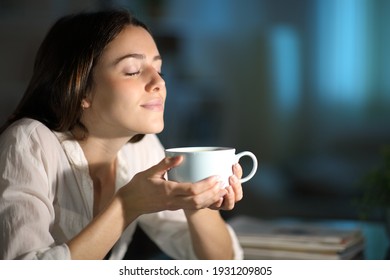 Relaxed woman smelling decaffeinated coffee in the night at home