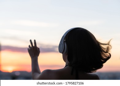 Relaxed woman with streaming hair wearing headphones listening to music on the beach at sunset. Back view, silhouette lonely girl trying to touch the sun  - Powered by Shutterstock