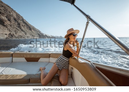 Relaxed woman in sun hat enjoying ocean voyage, sailing on the luxury yacht near the beautiful rocky coast during a sunset. Concept of a summer rest on the sea