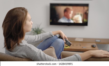 relaxed woman is watching films by tv screen in her home, sitting on a sofa in living room in holidays