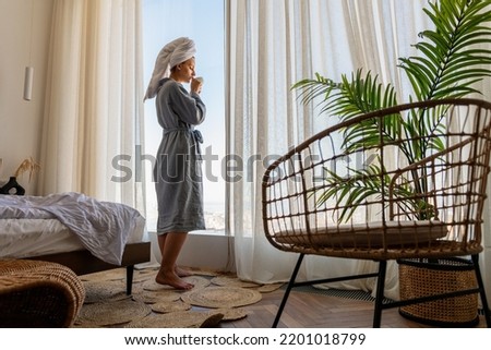 Relaxed woman wearing bath robe drinking coffee in hotel room in morning