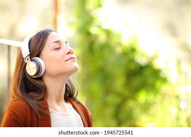 Relaxed Woman Wearing Headphones Breathing Fresh Air Meditating Listening To Music In A House Garden