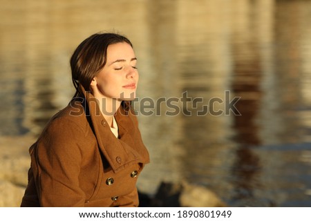 Relaxed woman in winter breathing fresh air sitting on the beach at sunset