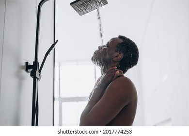 Relaxed young African-American man takes shower standing under hot water jets in contemporary unit in bathroom close side view - Powered by Shutterstock