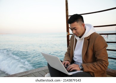 Relaxed Young Asian Man Using Laptop On The Beach.