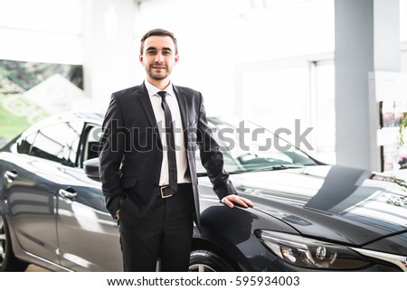 relaxed young businessman or salesman with hands crossed in front of car