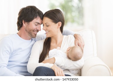 Relaxed young couple with cute little baby sitting on couch - Powered by Shutterstock