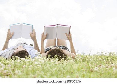 Relaxed young couple reading books while lying on grass against sky - Powered by Shutterstock