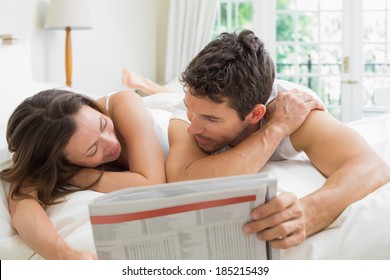 Relaxed Young Couple Reading Newspaper In Bed At Home